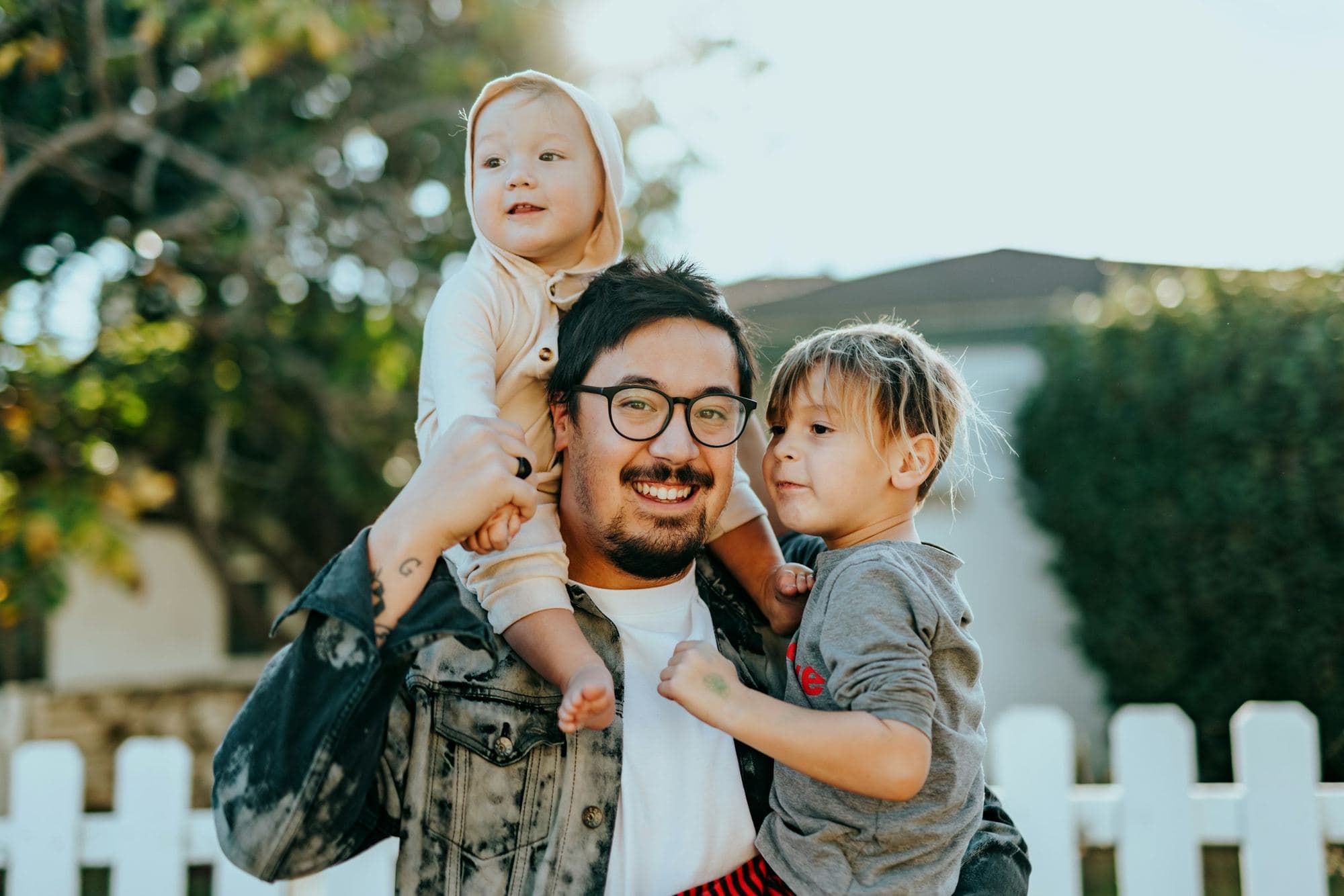 Un père souriant porte ses deux enfants devant leur nouvelle maison